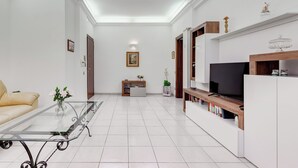 A modern living room with a glass coffee table, sofa, TV, and built-in shelves. - Cozy 2-Bedroom Flat with Balcony (Rome)