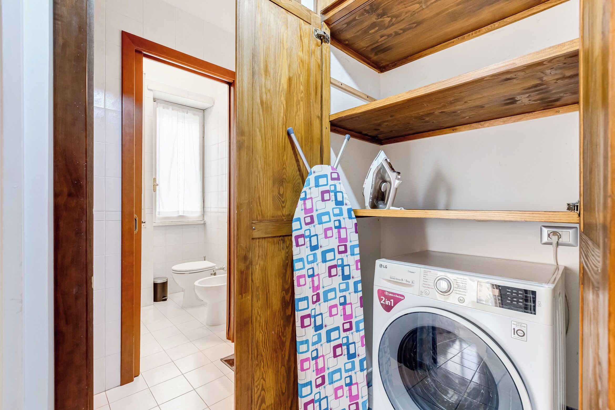 Un área de lavandería con lavadora, plancha y un tendedero estampado.