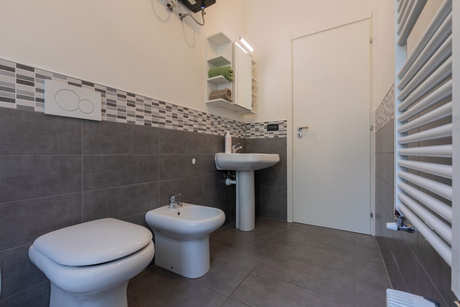 Un baño con inodoro, bidé y lavamanos, paredes de azulejos y una puerta.