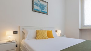 A neatly made bed with white and yellow pillows, a green throw blanket, and a nightstand with a lamp.