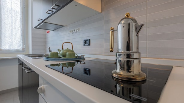 A modern kitchen with a black induction cooktop, a stainless steel espresso machine, and a green tea set on the counter.