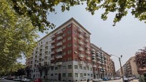 A multi-story residential building with balconies, a parking lot, and a clear sky.