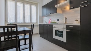 A modern kitchen with dark cabinets, a white countertop, and a window with sheer curtains.