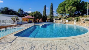 A swimming pool with a stone-tiled deck, surrounded by a white fence, and a small building with a red roof in the background. - Fabulous apartment in beautiful Quinta do Paraiso (Carvoeiro)