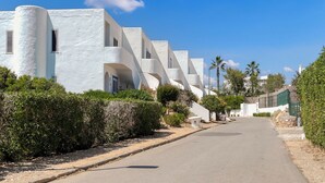 A row of white buildings with balconies, a clear sky, and a road with greenery on the sides. - Fabulous apartment in beautiful Quinta do Paraiso (Carvoeiro)
