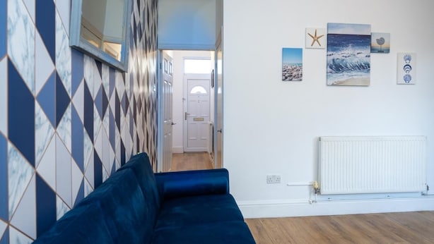 A room with a blue sofa, a patterned wall, and a white radiator. - 3br-7guests-freeparking-pets-towncentre (Stoke-on-Trent)