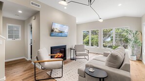 Un salon moderne doté d’une cheminée, de sièges confortables et de grandes fenêtres donnant sur un paysage verdoyant.