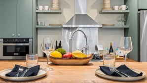 Une cuisine moderne dotée d’un îlot central, d’une hotte en acier inoxydable et de divers ustensiles de cuisine rangés sur des étagères.