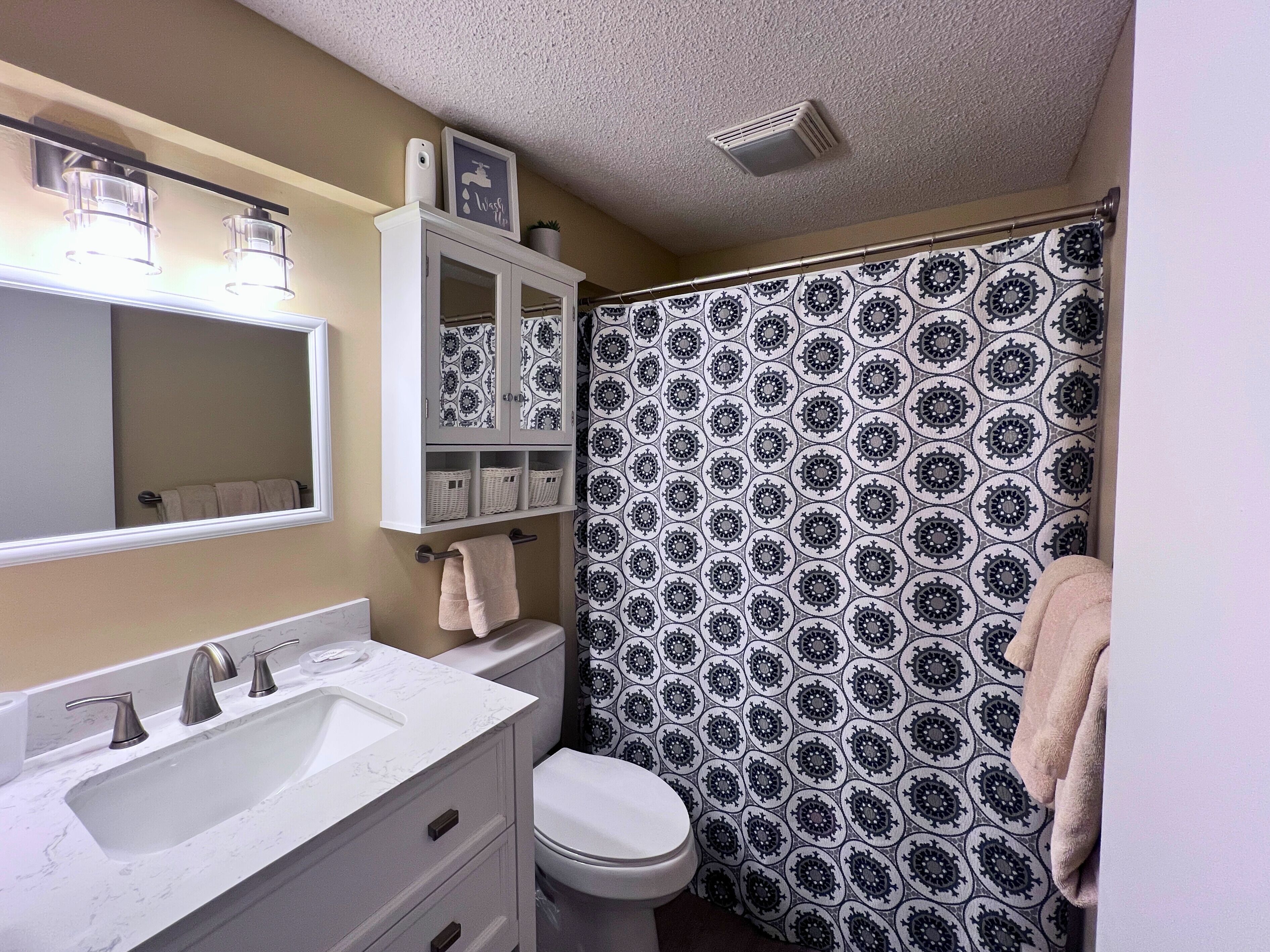 A bathroom with a white sink, vanity, and toilet. There is a shower curtain with a black and white pattern.