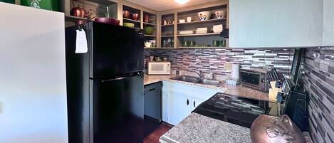A compact kitchen with a black refrigerator, white cabinets, a microwave, and a sink.