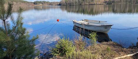 A boat tied to a dock with a red buoy, surrounded by trees and calm water.