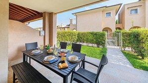 Patio esterno con tavolo apparecchiato per un pasto, circondato da sedie e affaccio su una zona residenziale.