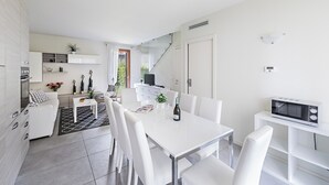 Una cucina moderna con mobili bianchi, un'area pranzo con tavolo e sedie bianche e un forno a microonde integrato.