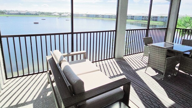 Un espacio al aire libre cubierto con vista a un lago, una zona de estar con mesa y una barandilla.