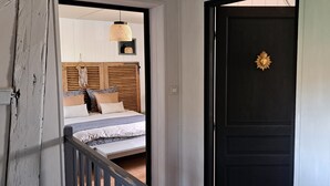 A bedroom with a bed, a hanging light fixture, and a black door with a gold emblem. - La Ferme des Pins, relaxation with family and friends, 15 minutes from the beach (Carly)