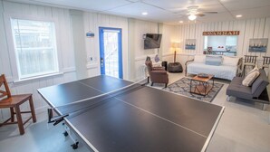 Una habitación con mesa de ping pong, sofá, sillón, lámpara y televisor.