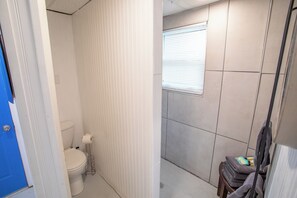 Un baño pequeño y estrecho con inodoro, una ventana con persianas y un perchero con toallas.
