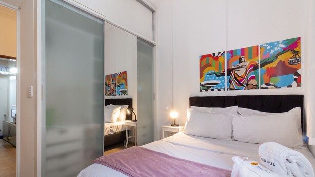 Una habitación de hotel con cama, mesita de noche, lámpara, ventana con vistas y puerta corredera.