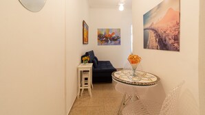 Un estrecho pasillo con un sofá azul oscuro, una mesita blanca con un jarrón de flores y una mesa redonda con un adorno en la parte superior.