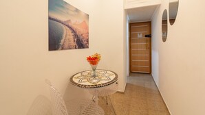 Un pasillo con una mesa redonda, un florero con flores, un cuadro enmarco y una puerta de madera.
