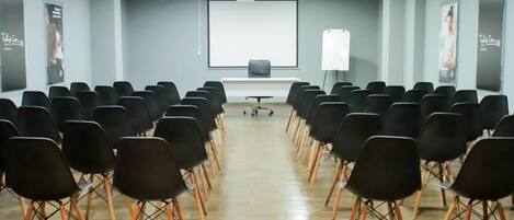 A conference room with rows of black chairs, a projector screen, and a whiteboard.