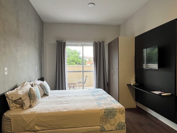 Een slaapkamer met een bed, een televisie aan de muur en een balkon met uitzicht op groen.