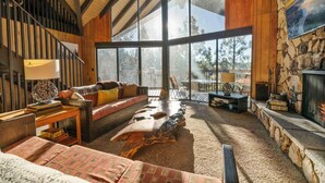 A cozy living room with a large window, a stone fireplace, and a wooden ceiling.