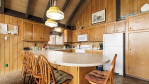 A kitchen with wooden cabinets, a central island with chairs, a microwave, and a refrigerator.