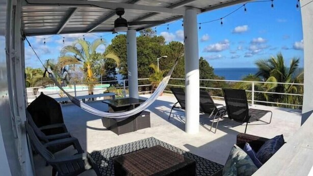 A covered outdoor seating area with a hammock, lounge chairs, and a view of the ocean.