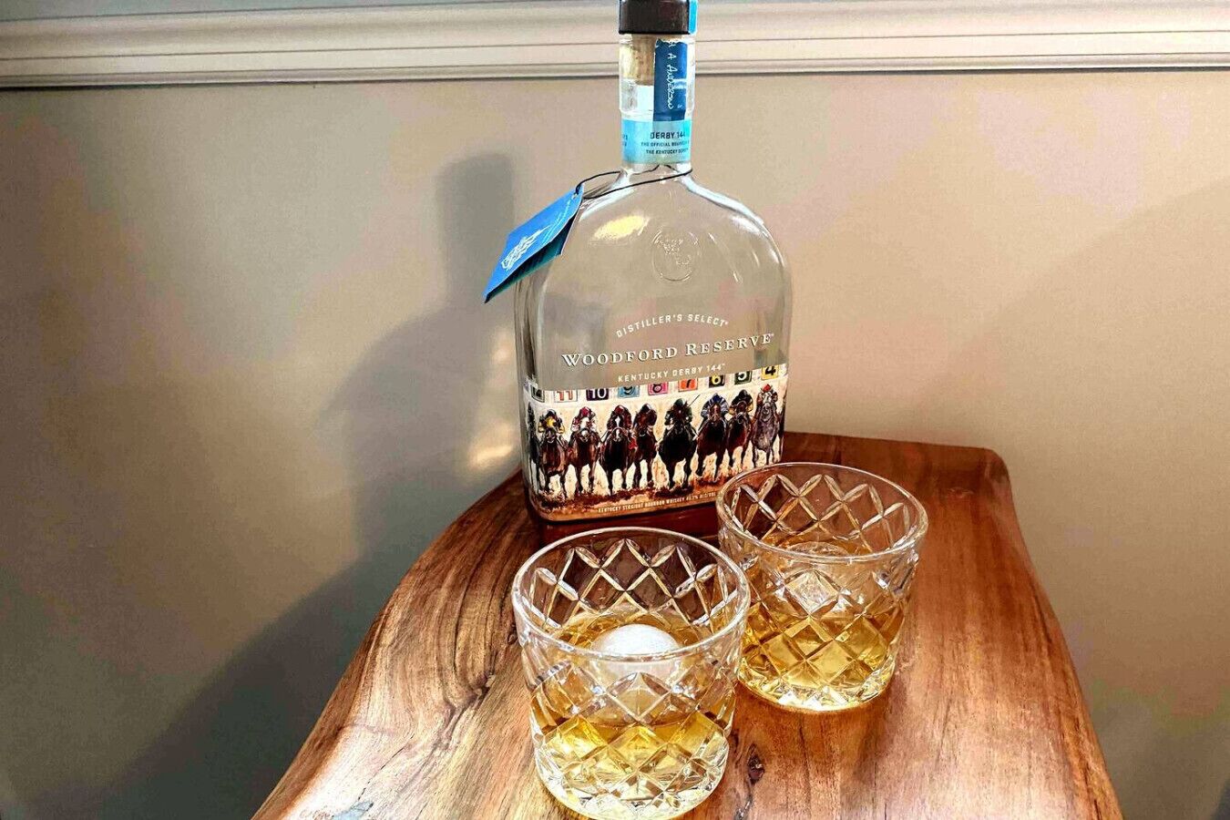 Una botella de whisky Woodford Reserve Kentucky Derby 144 sobre una mesa de madera con dos vasos.