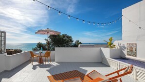 A rooftop terrace with a table and chairs, a string of lights, and a view of the sea. - Ocean View Apartment with rooftop terrace (Carvoeiro)