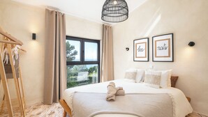 A neatly made bed with a towel, a wooden drying rack, and a large window with curtains. - Ocean View Apartment with rooftop terrace (Carvoeiro)