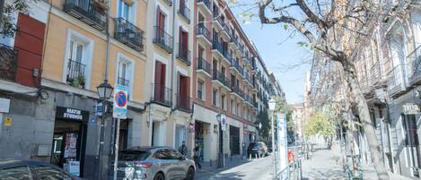 A street with multi-story buildings, a parked car, and a pedestrian.