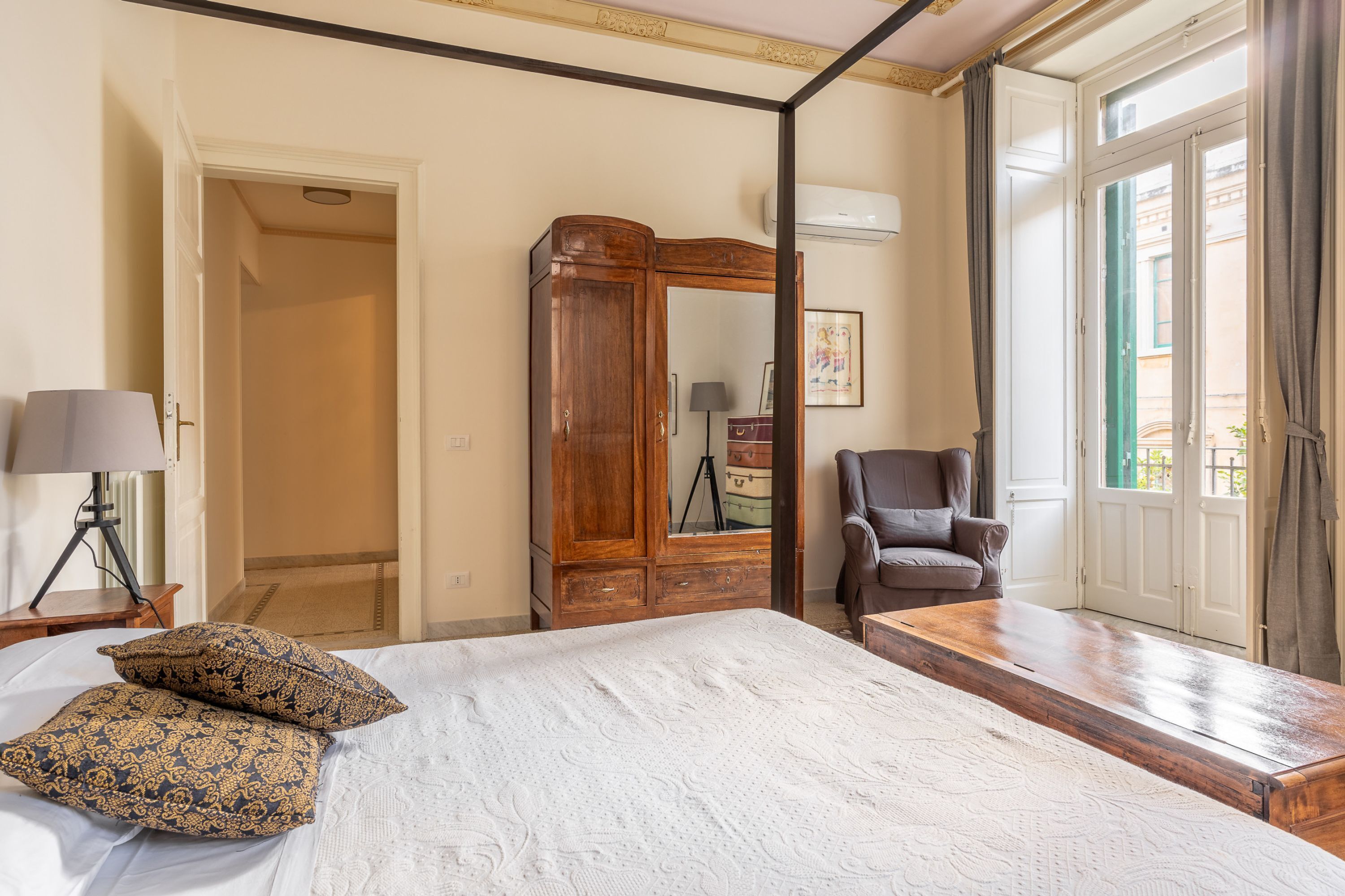 A bedroom with a large bed, a wooden wardrobe, a chair, and a desk.