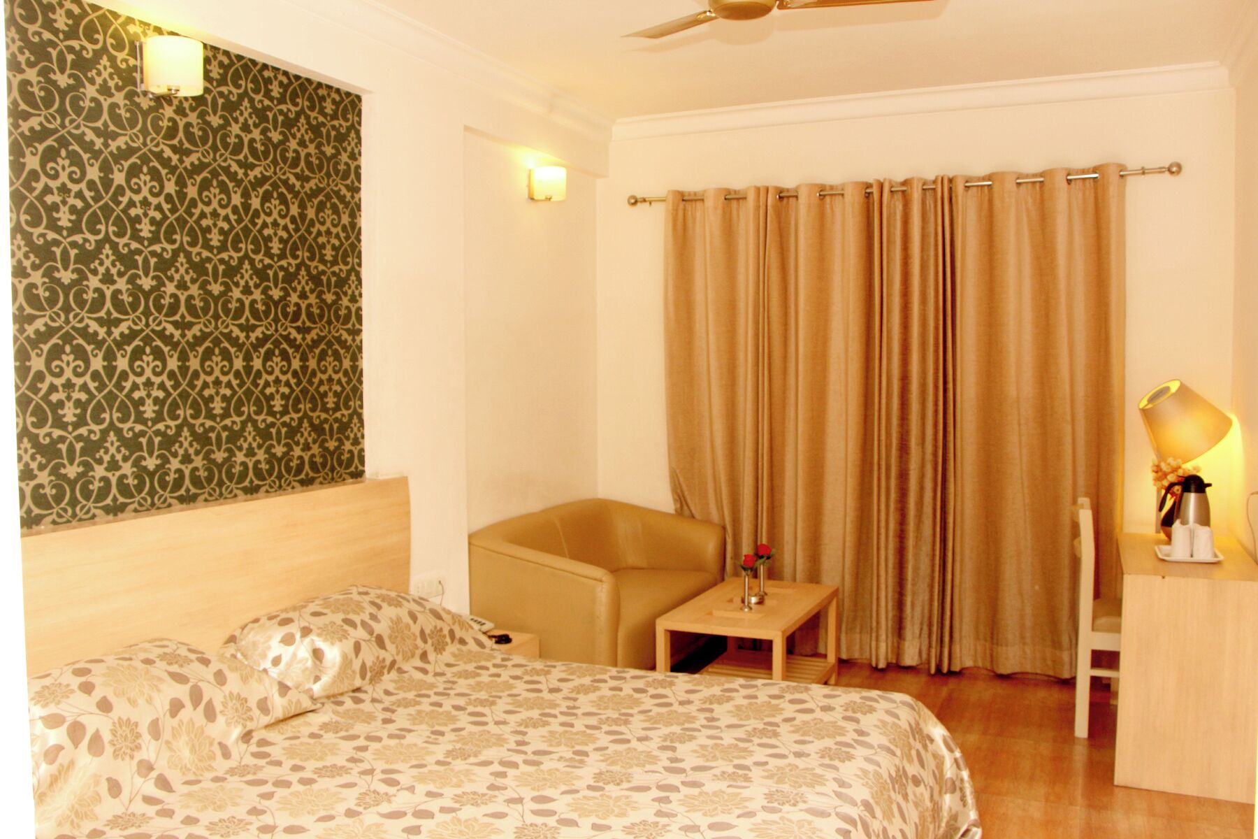 A hotel room with a bed, a chair, a nightstand, a lamp, and a curtain.