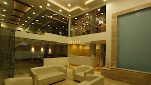 A modern lobby with a glass wall, a reception desk, and a pool area. - Hotel Crown Palace (Prayagraj)