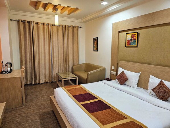 A hotel room with a bed, a chair, a small table, a coffee maker, and curtains. - Hotel Crown Palace (Prayagraj)