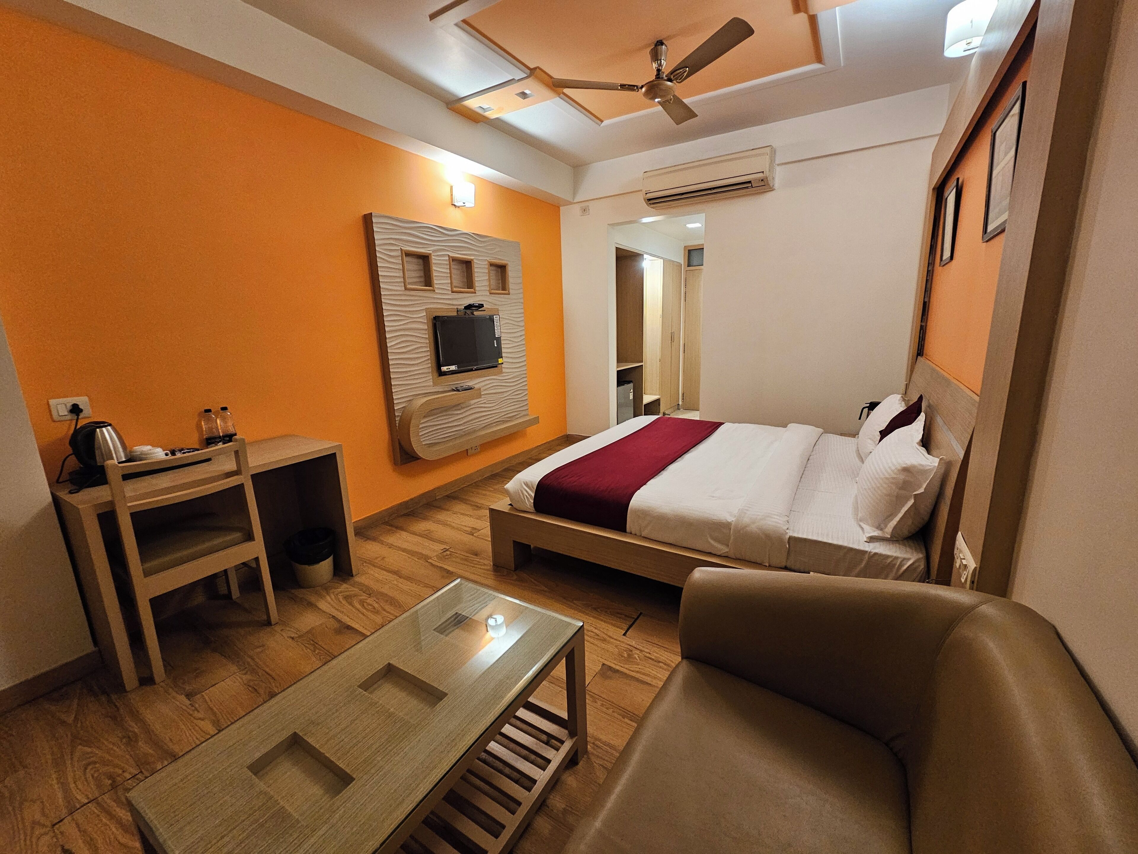 Habitación de hotel con cama, escritorio, silla, televisor montado en la pared y ventilador de techo.