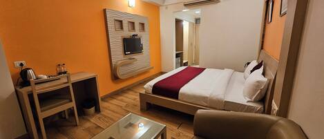 Habitación de hotel con cama, escritorio, silla, televisor montado en la pared y ventilador de techo.