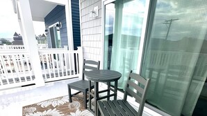 En balkon med hvid gelænder, et bord, to stole og en måtte med blomstermønster.