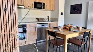Une cuisine moderne avec des meubles en bois, un four à micro-ondes encastré et un lave-vaisselle. On y trouve une table à manger avec des chaises et un panier de fruits.