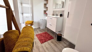 Une salle de bain moderne avec un banc en bois, un tapis rouge, un lavabo blanc et un miroir.