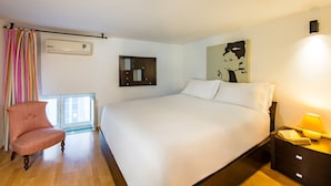 Een hotelkamer met een groot bed, een stoel, een nachtkastje met een lamp, een wandairconditioner, een spiegel en een raam met gordijnen.