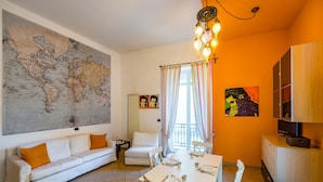 Een woonkamer met een grote wereldkaart, een witte bank, een eettafel gedekt voor vier personen en een televisie op een houten kast.