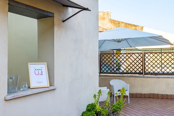 A balcony with a white chair, a framed welcome sign, and a large umbrella.