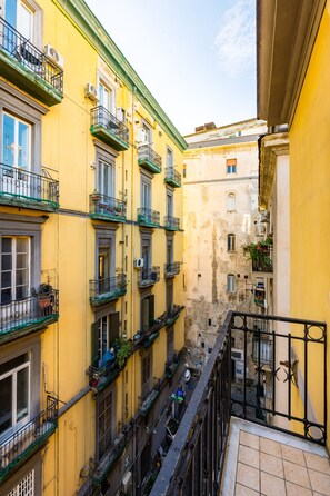 A narrow street between yellow buildings with balconies, some with plants.