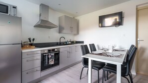Una cocina moderna con horno empotrado, microondas y refrigerador de acero inoxidable. Hay una mesa de comedor con sillas negras y un televisor de pantalla plana montado en la pared.