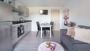 Una cocina moderna con comedor, un sofá gris y un televisor de pantalla plana en la pared.