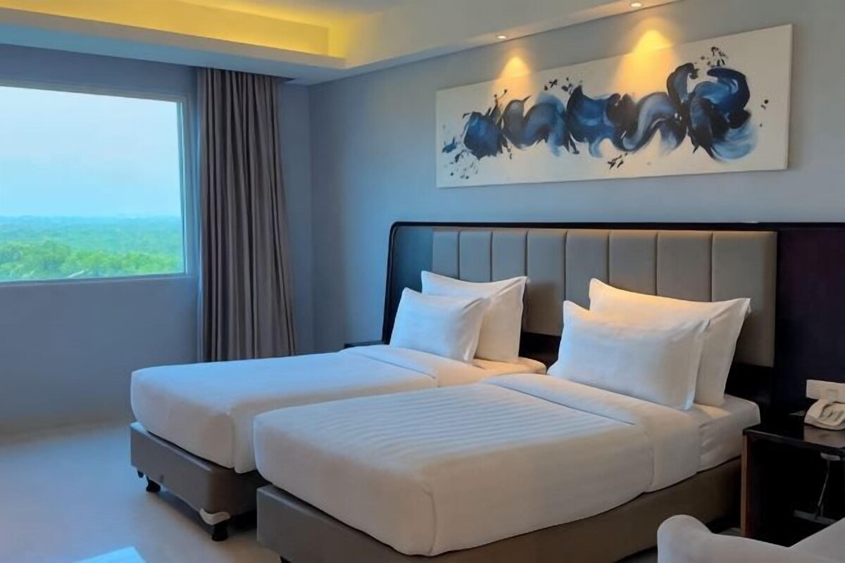 Habitación de hotel con dos camas, un ventanal grande y un cuadro en la pared.