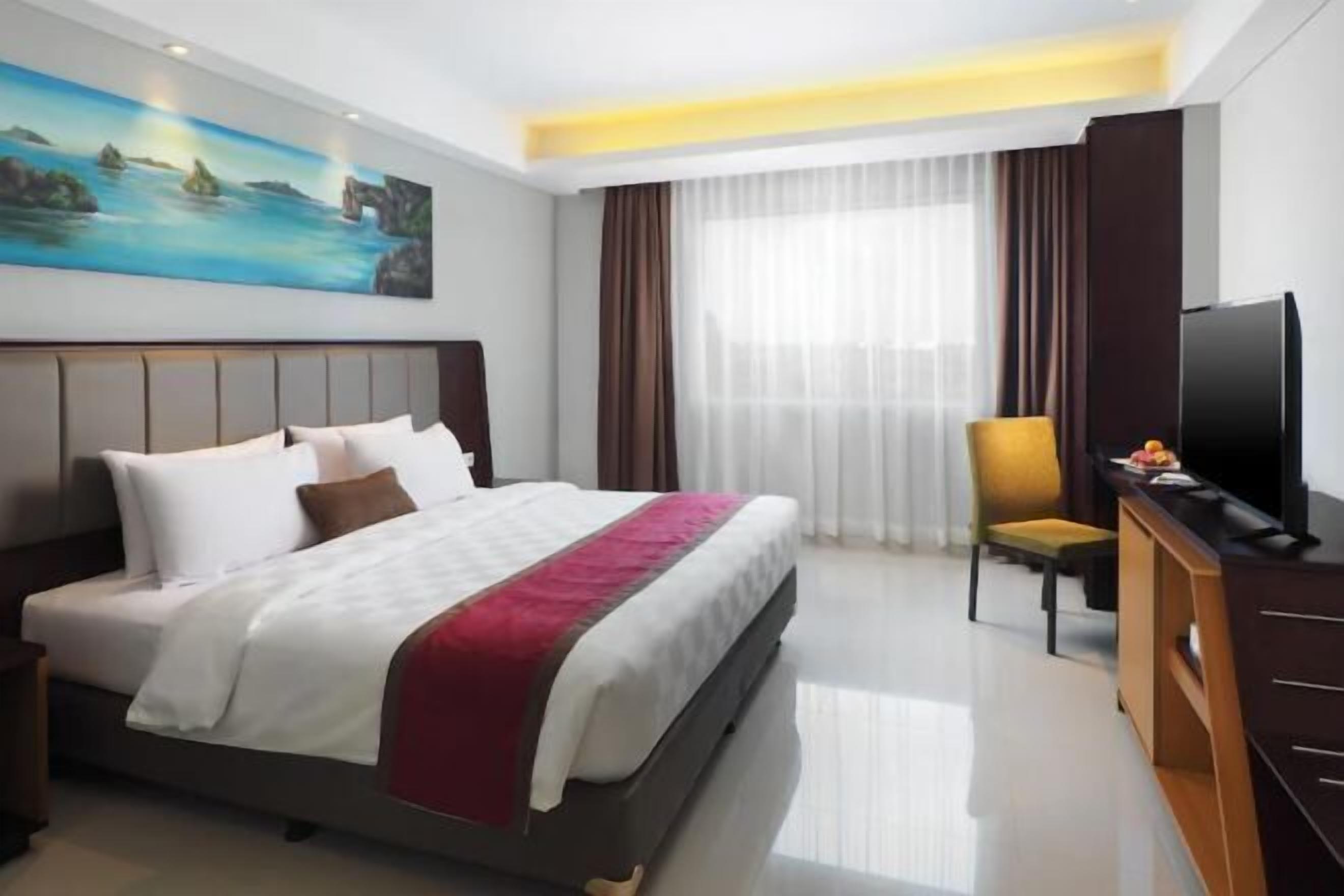 A hotel room with a large bed, a television, a desk, and a painting on the wall.